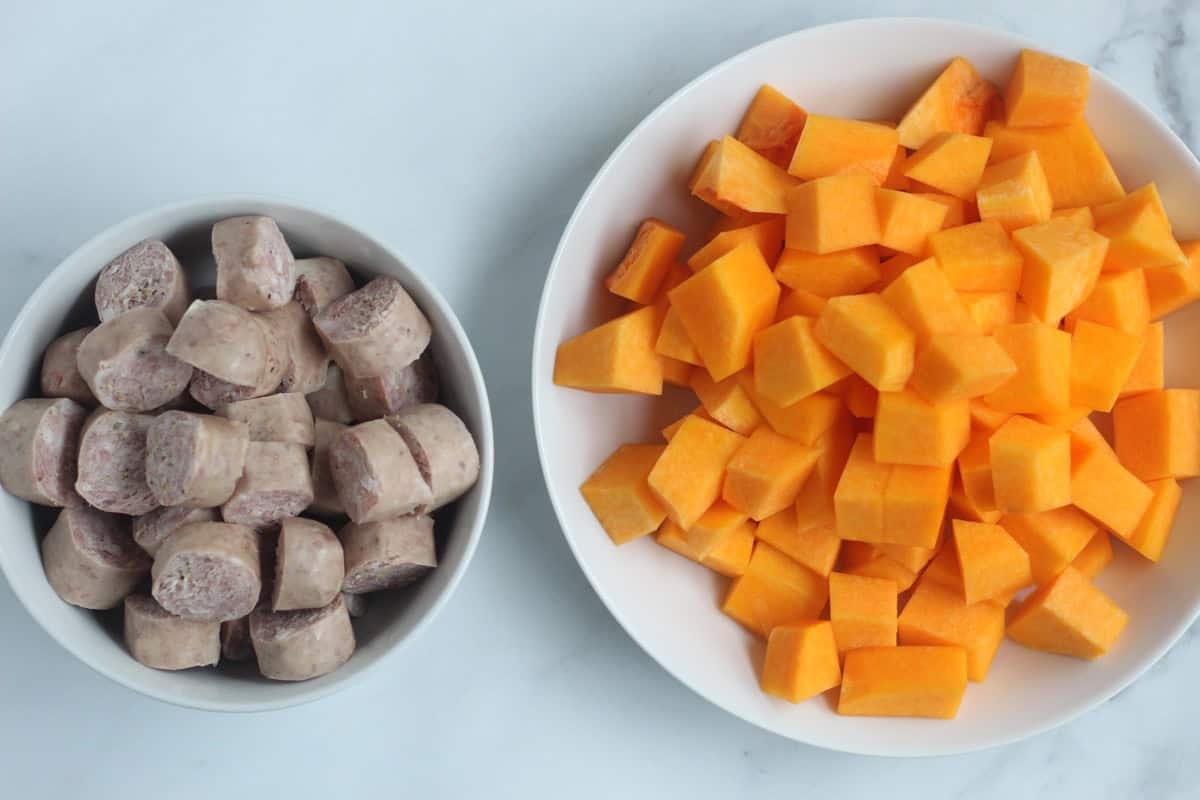 Sliced sausage and cubed butternut squash in bowls.