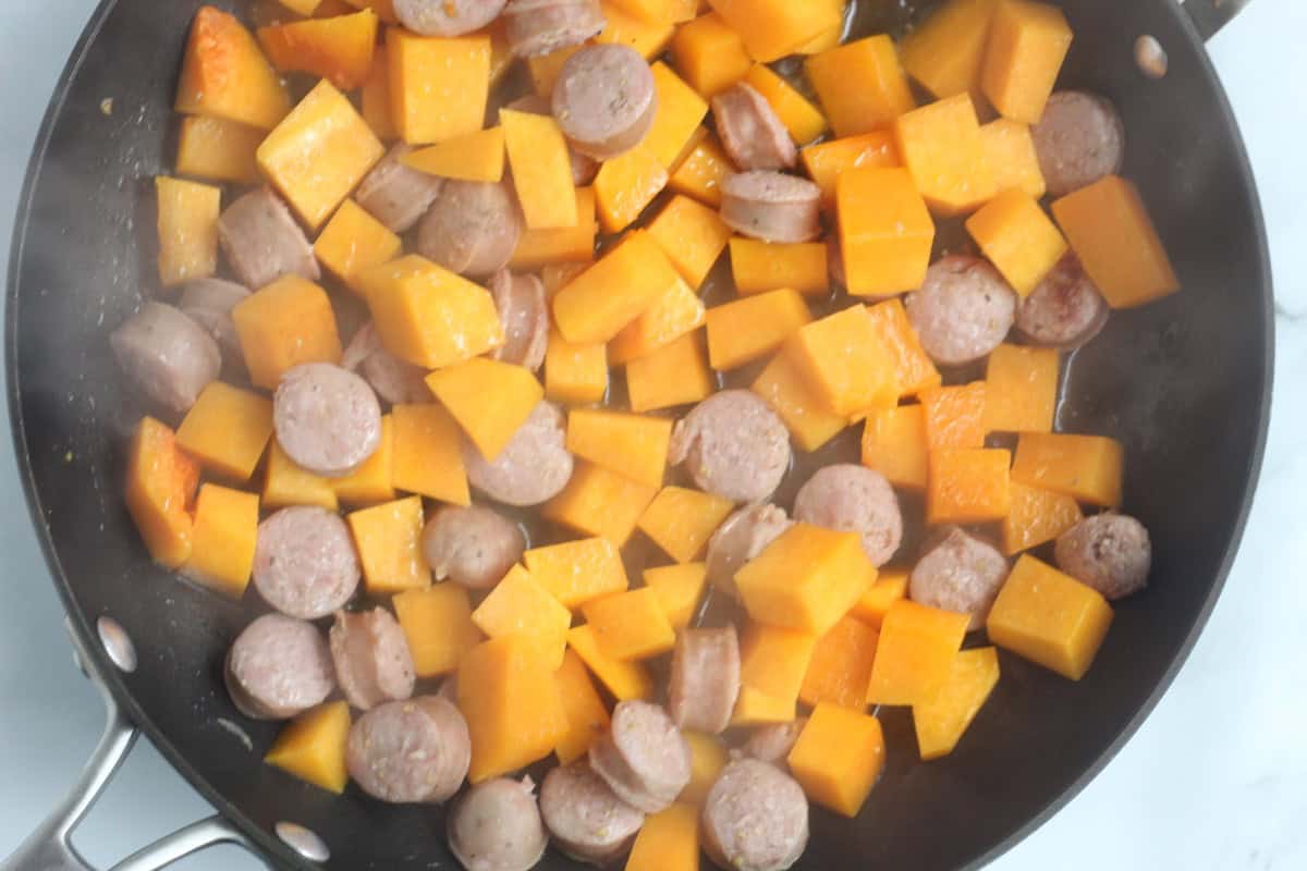 Sausage and butternut squash cooking in a skillet.