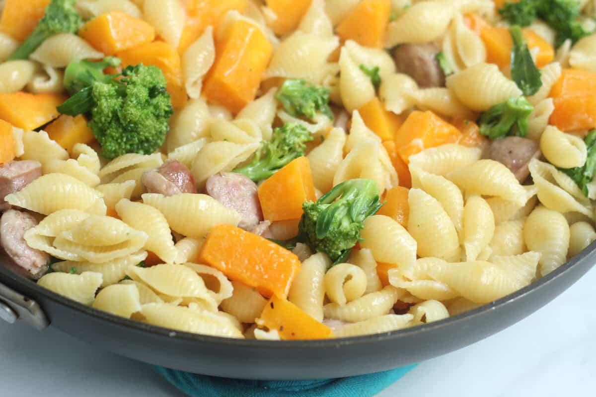 Butternut squash pasta with sausage and broccoli in a skillet.