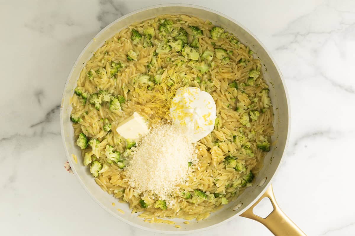 Greek yogurt, Parmesan, butter, and lemon zest on broccoli orzo in a skillet.