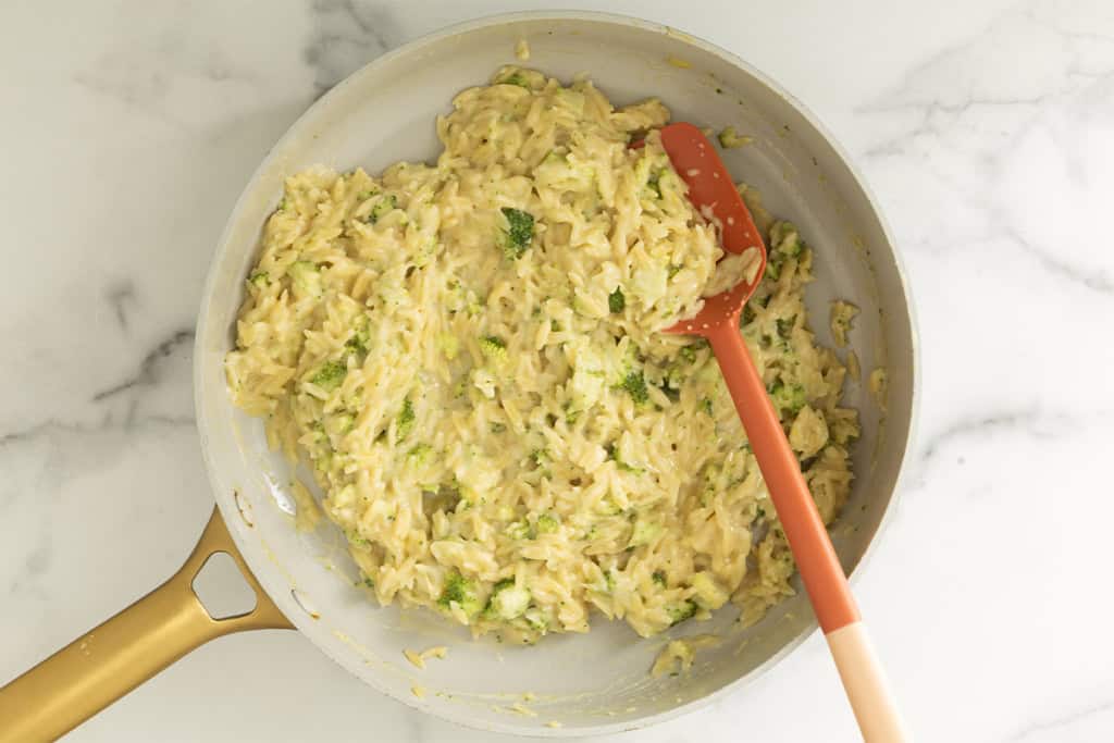 Creamy broccoli orzo stirred together in a skillet with an orange spatula.