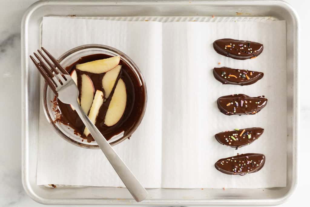 Apple slices dipped in melted chocolate and topped with sprinkles.