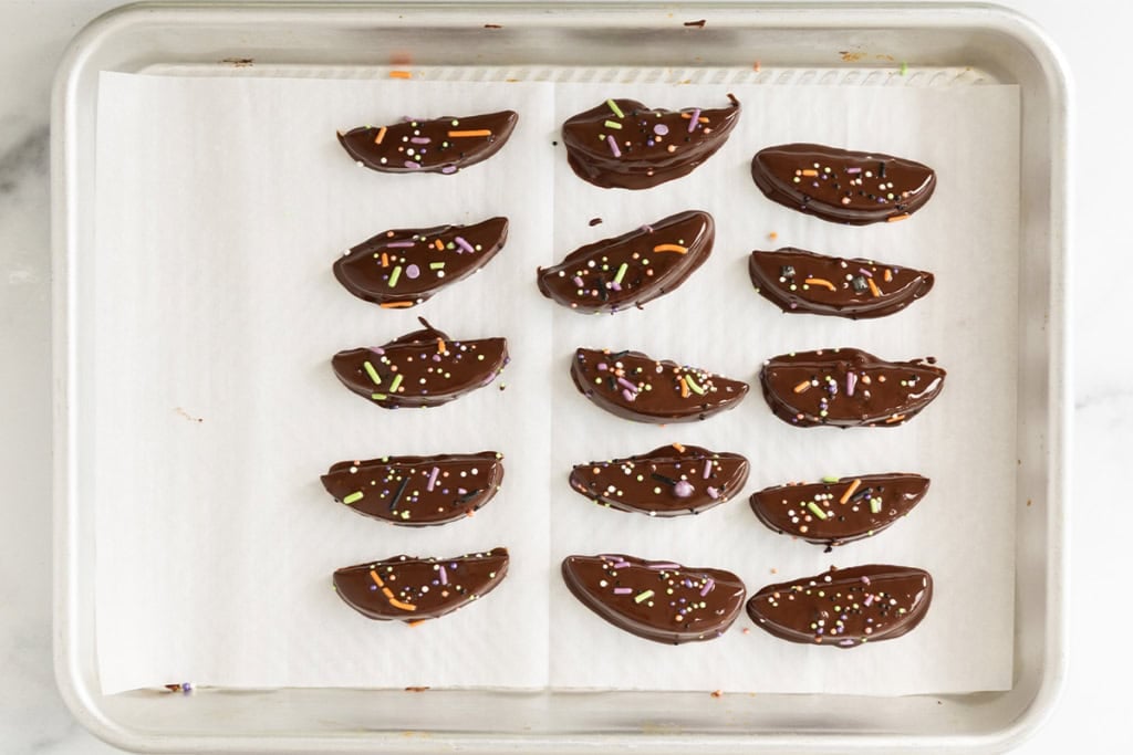 Chocolate covered apple slices with sprinkles on a parchment-lined baking sheet.