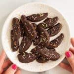 Chocolate covered apple slices with sprinkles on a plate.