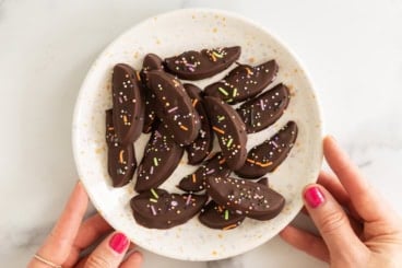Chocolate covered apple slices with sprinkles on a plate.