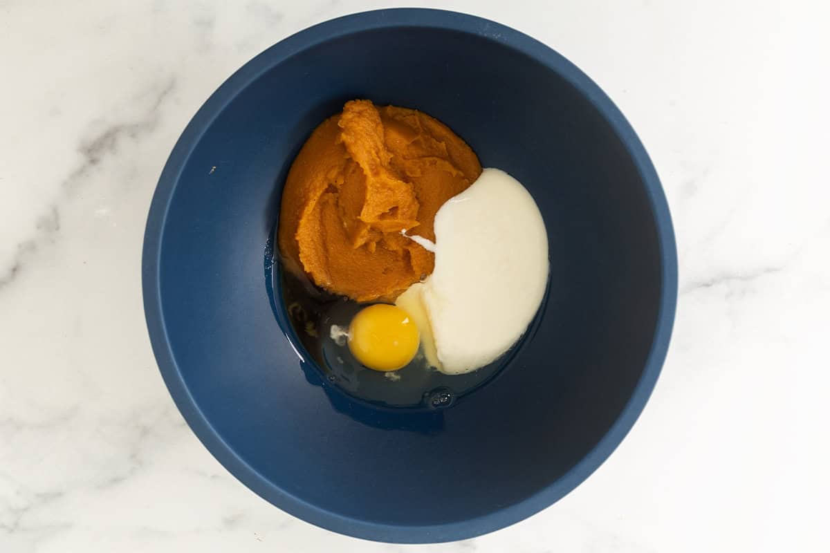 Pumpkin puree, yogurt, and egg in a blue mixing bowl.