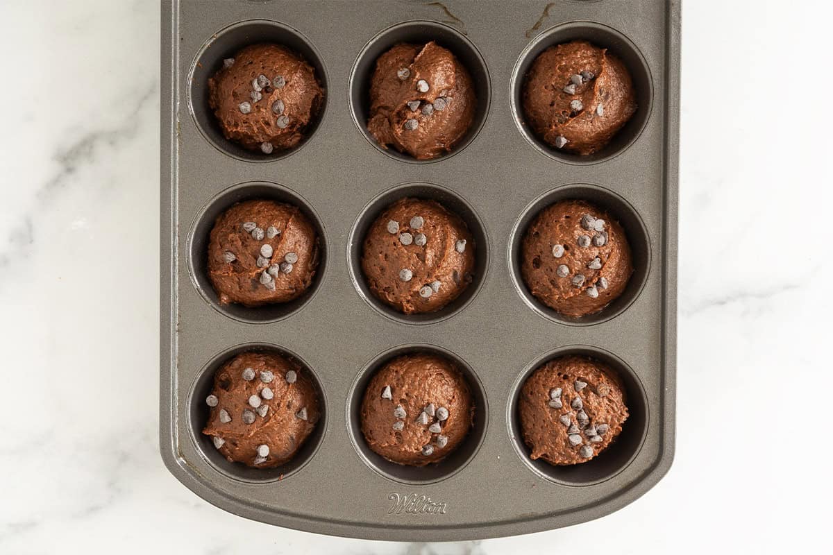 Chocolate pumpkin muffin batter portioned into a mini muffin pan and topped with chocolate chips.