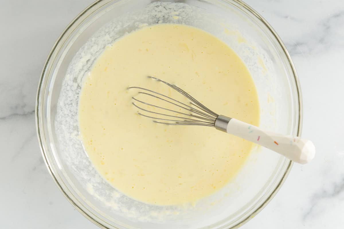 Wet ingredients for cinnamon swirl pancakes in glass bowl with whisk.