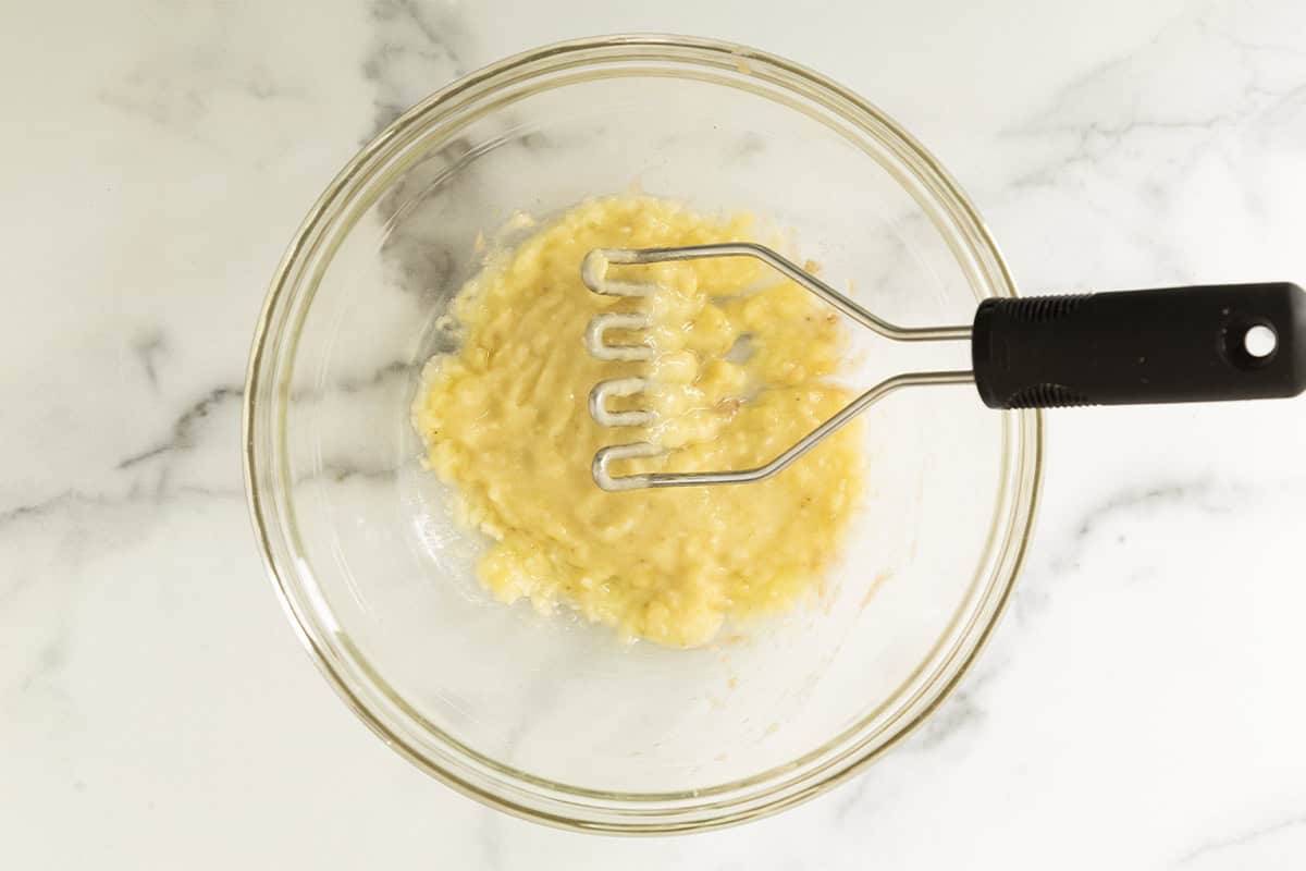Mashed banana in glass bowl for Eggless banana muffins.