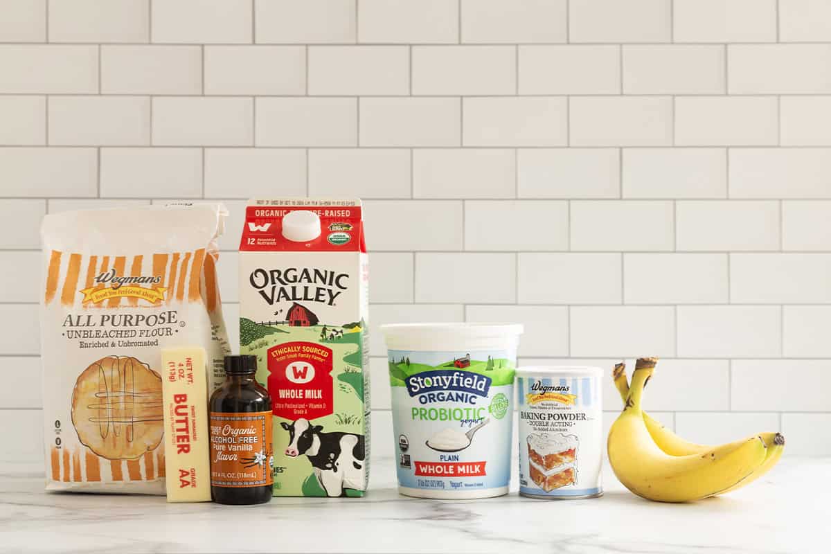 Flour, butter, vanilla, milk, yogurt, baking powder, and bananas for eggless banana pancakes.