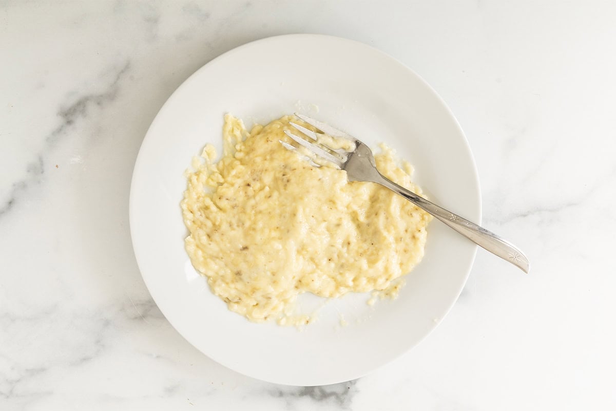 Mashed banana on a white plate with a fork.