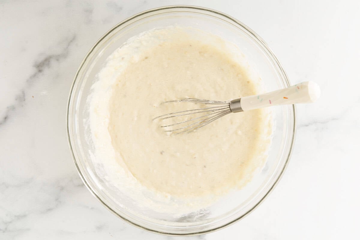 Eggless banana pancake batter in a glass mixing bowl with a whisk.