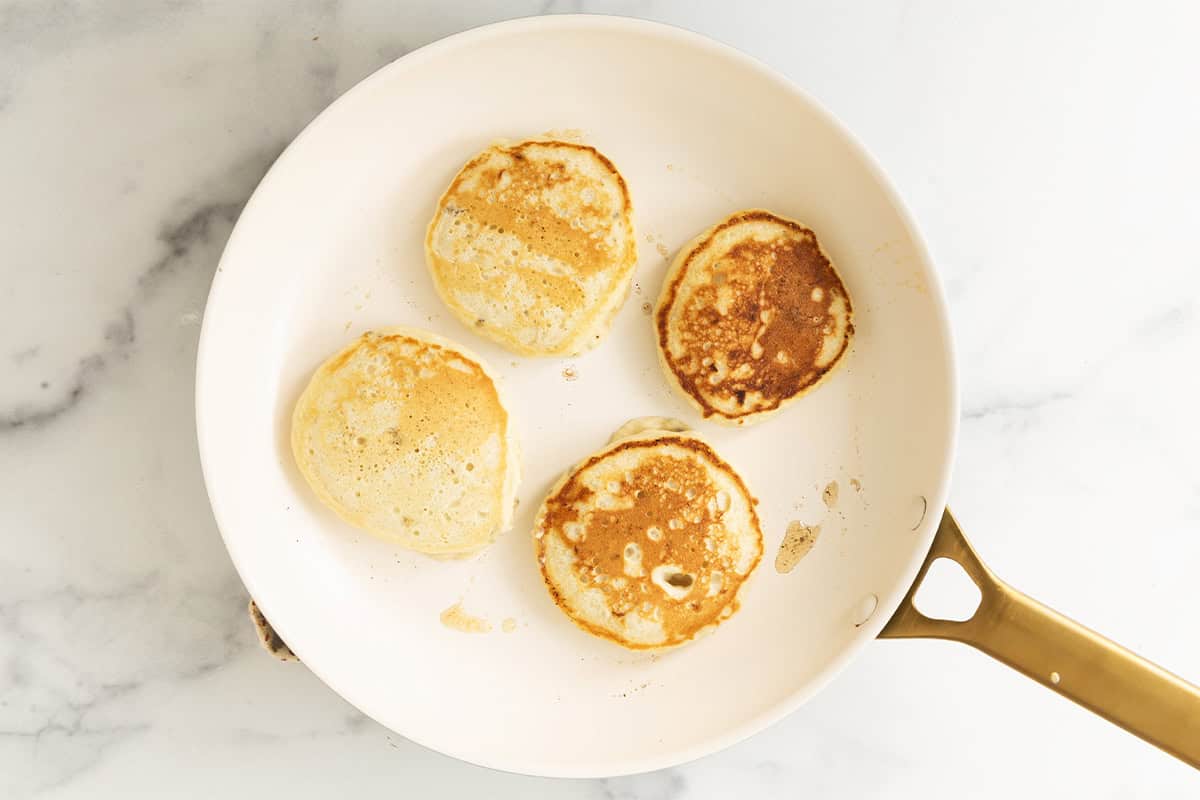 Eggless banana pancakes cooking in a skillet.