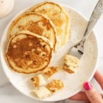 Eggless banana pancakes on a plate with bite-size pieces and a fork.