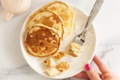 Eggless banana pancakes on a plate with bite-size pieces and a fork.