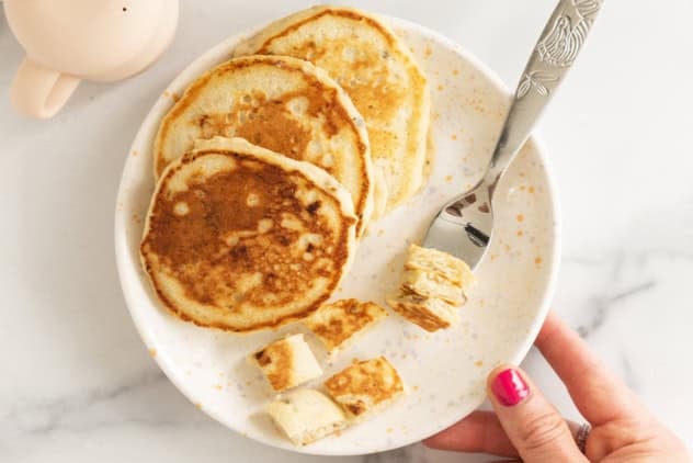 Eggless banana pancakes on a plate with bite-size pieces and a fork.