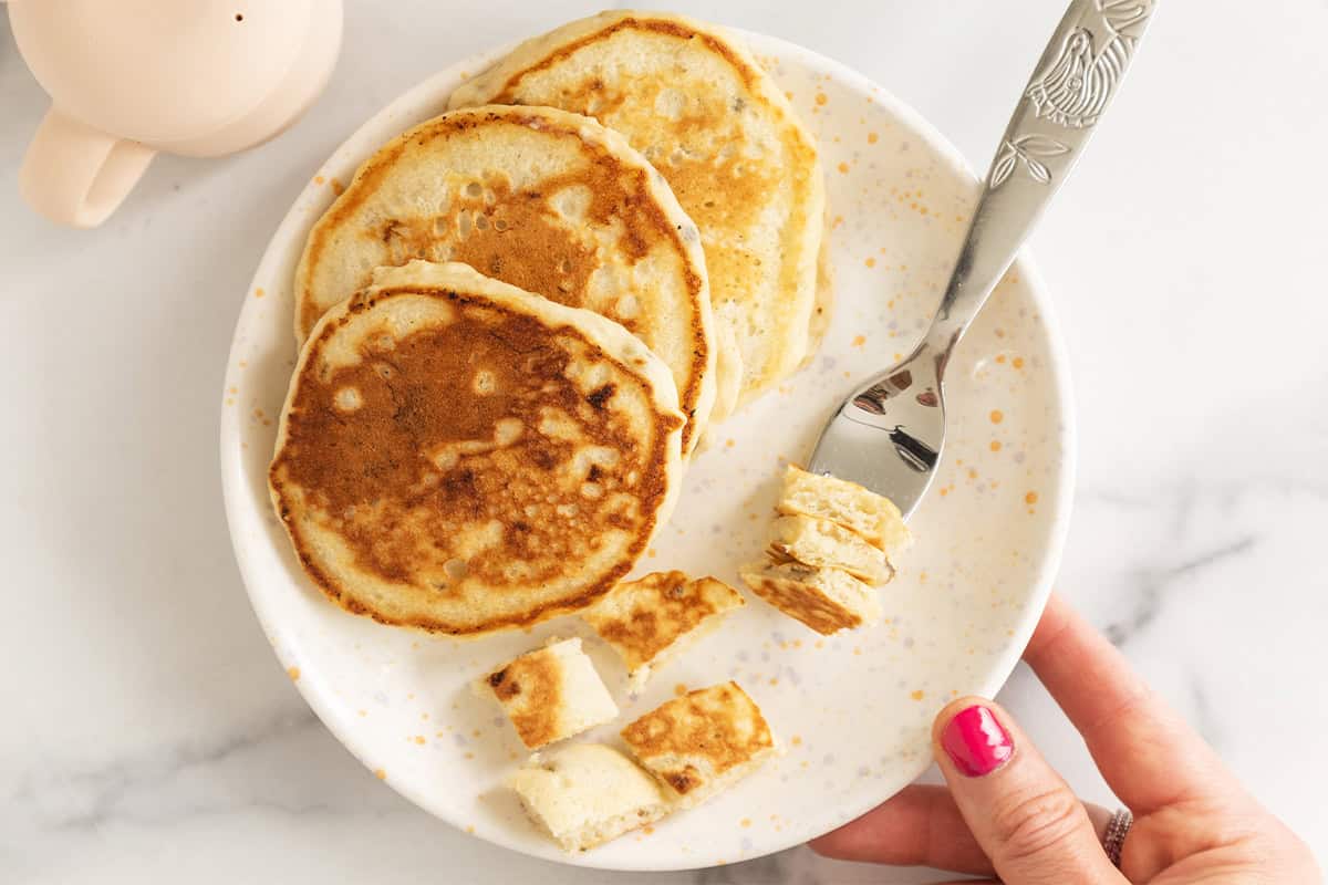Eggless banana pancakes on a plate with bite-size pieces and a fork.