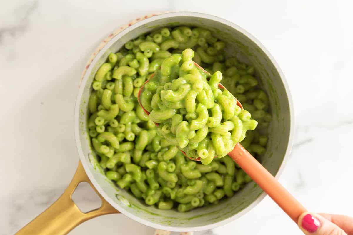 Green mac and cheese lifted from a pot with a serving spoon.