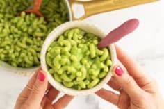 A bowl of green mac and cheese held over a pot of pasta.