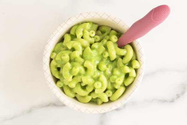 A bowl of creamy green mac and cheese with a pink spoon.