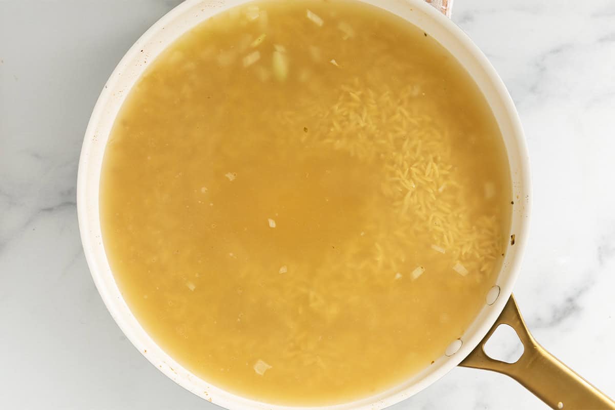 Broth with orzo in pan for lemon orzo chicken.