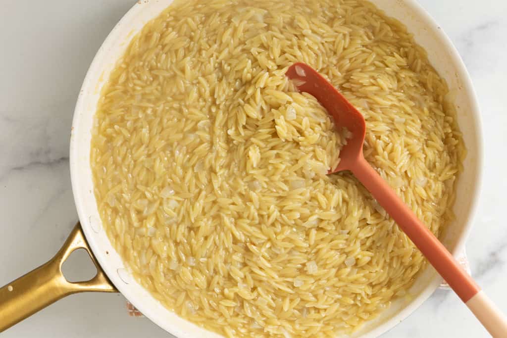 Spoon stirring orzo in pan for lemon orzo chicken.
