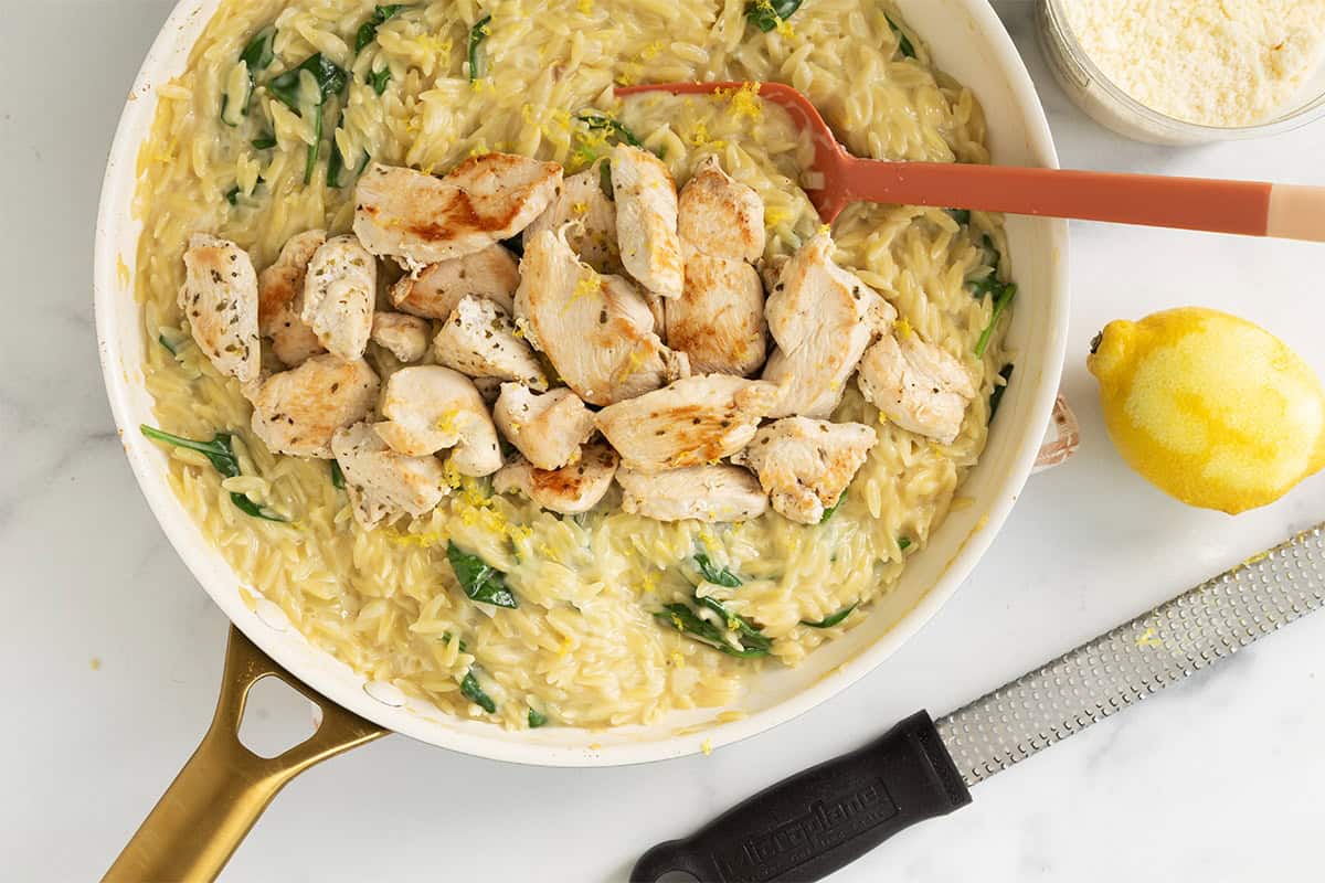 Adding chicken to orzo in pan for lemon orzo chicken.