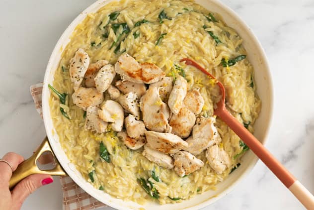 Lemon orzo chicken in pan with red spoon.