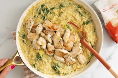 Lemon orzo chicken in pan with red spoon and orzo bag on side.