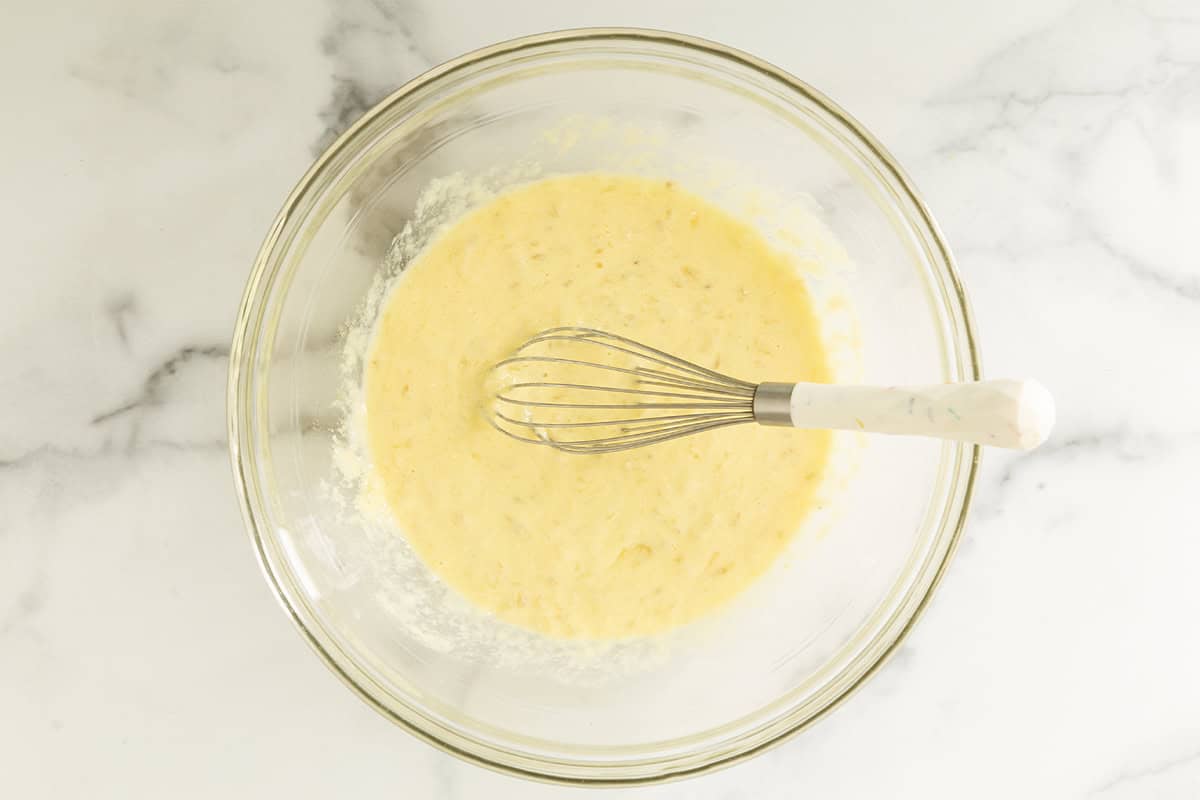 Mashed banana, yogurt, eggs, melted butter, and vanilla whisked in a glass bowl.