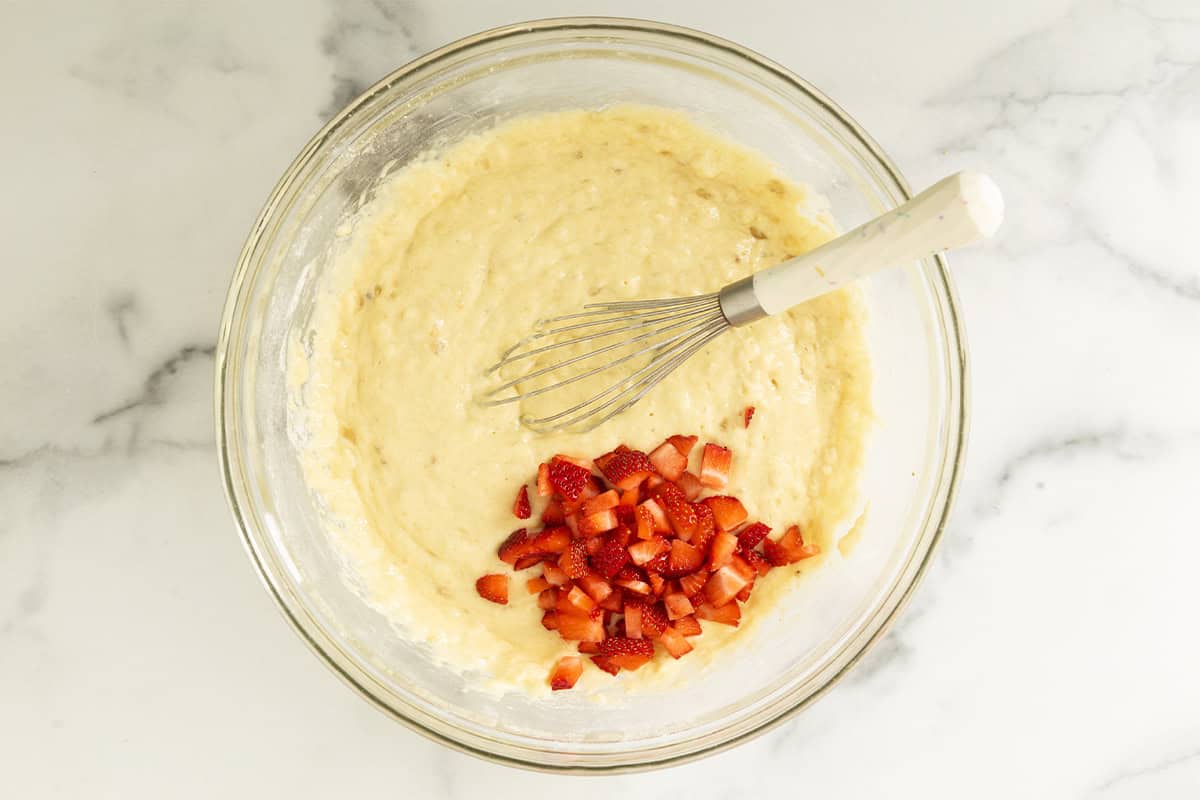 Diced strawberries added to banana pancake batter in a glass bowl.