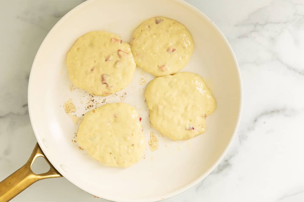Strawberry banana pancake batter cooking in a skillet.