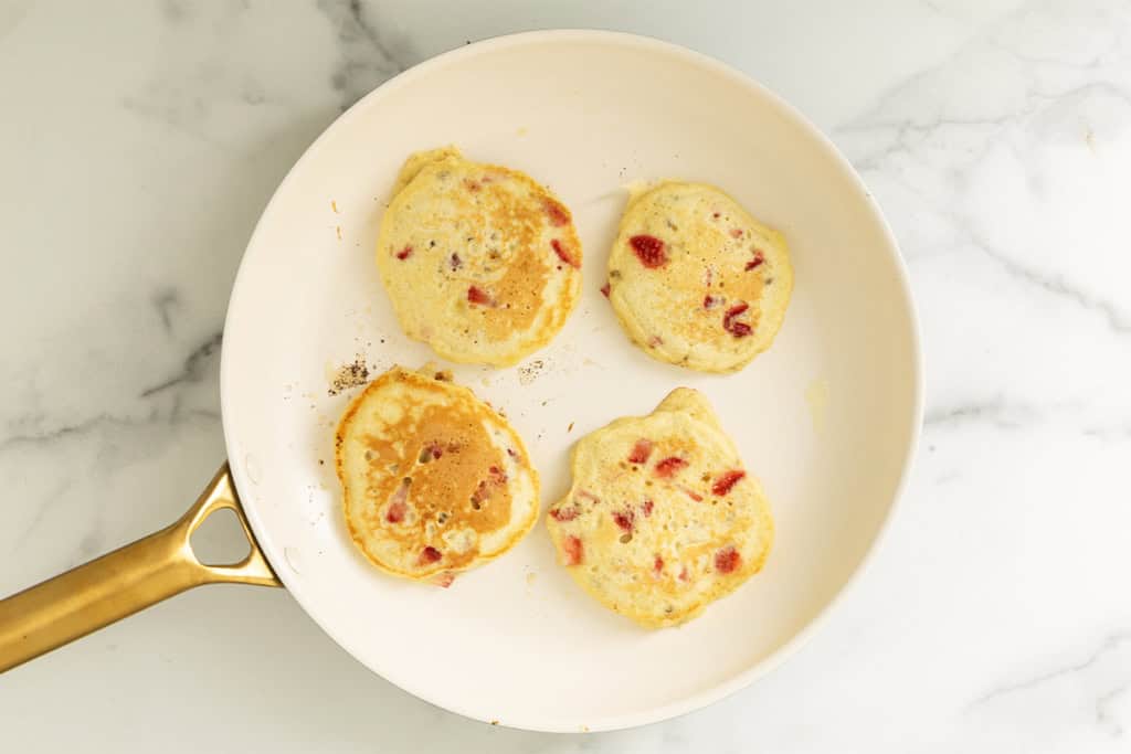 Cooked strawberry banana pancakes in a skillet.