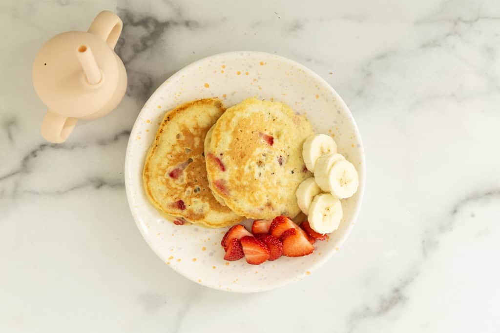 Strawberry banana pancakes served with sliced bananas and strawberries.