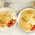 Strawberry banana pancakes on two plates with sliced bananas and strawberries.