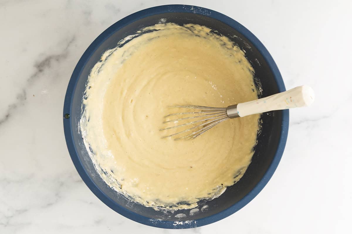 Vanilla muffin batter mixed in a blue bowl with a whisk.