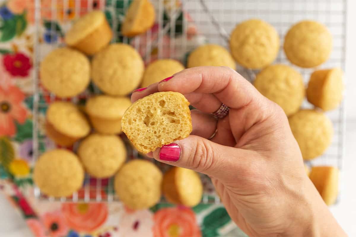 A halved mini vanilla muffin held over a cooling rack of muffins.
